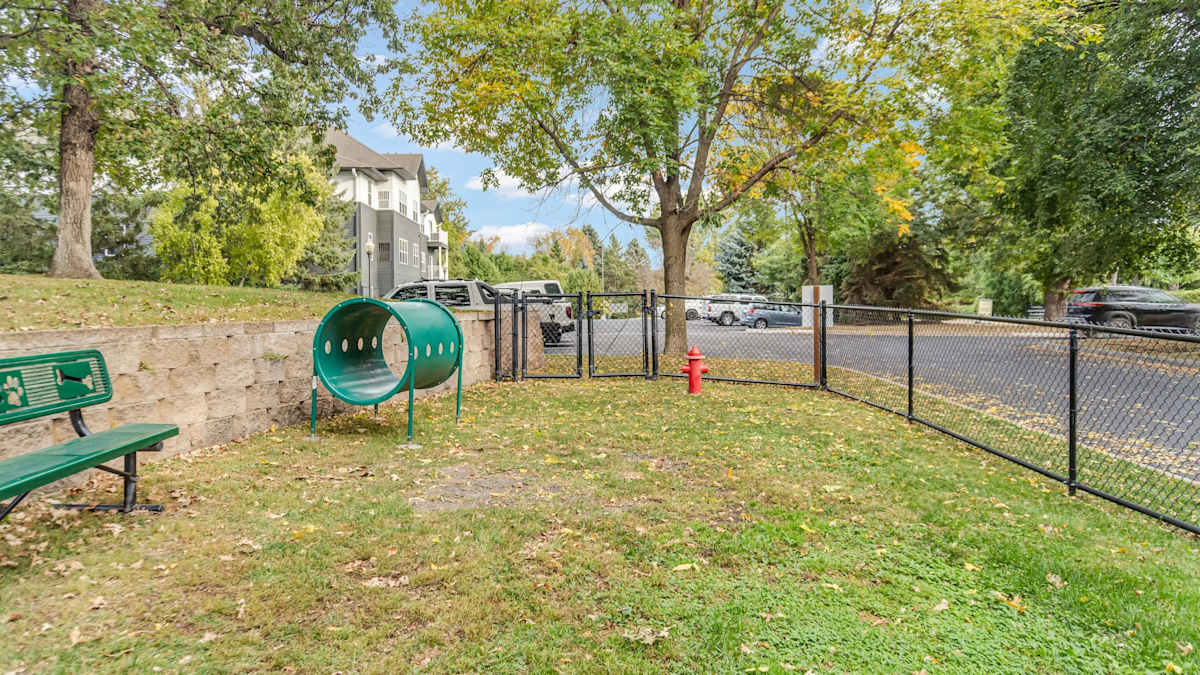 Fenced dog run with grass, a bench, and play equipment