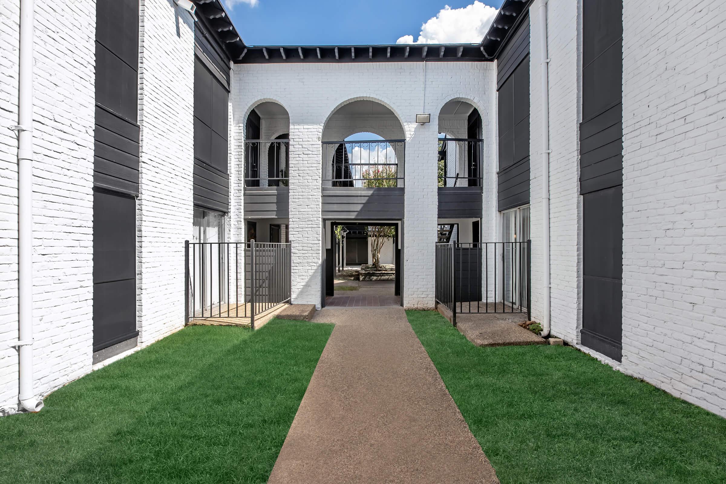 Maravilla courtyard walkway through a white brick archway.