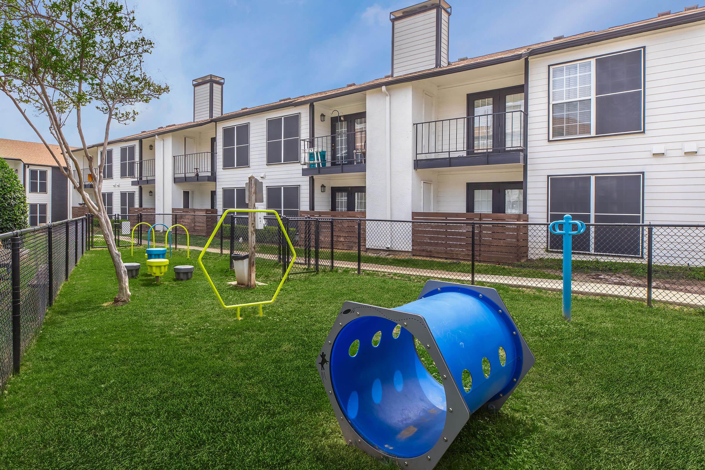 Fenced bark park with grass and dog play equipment