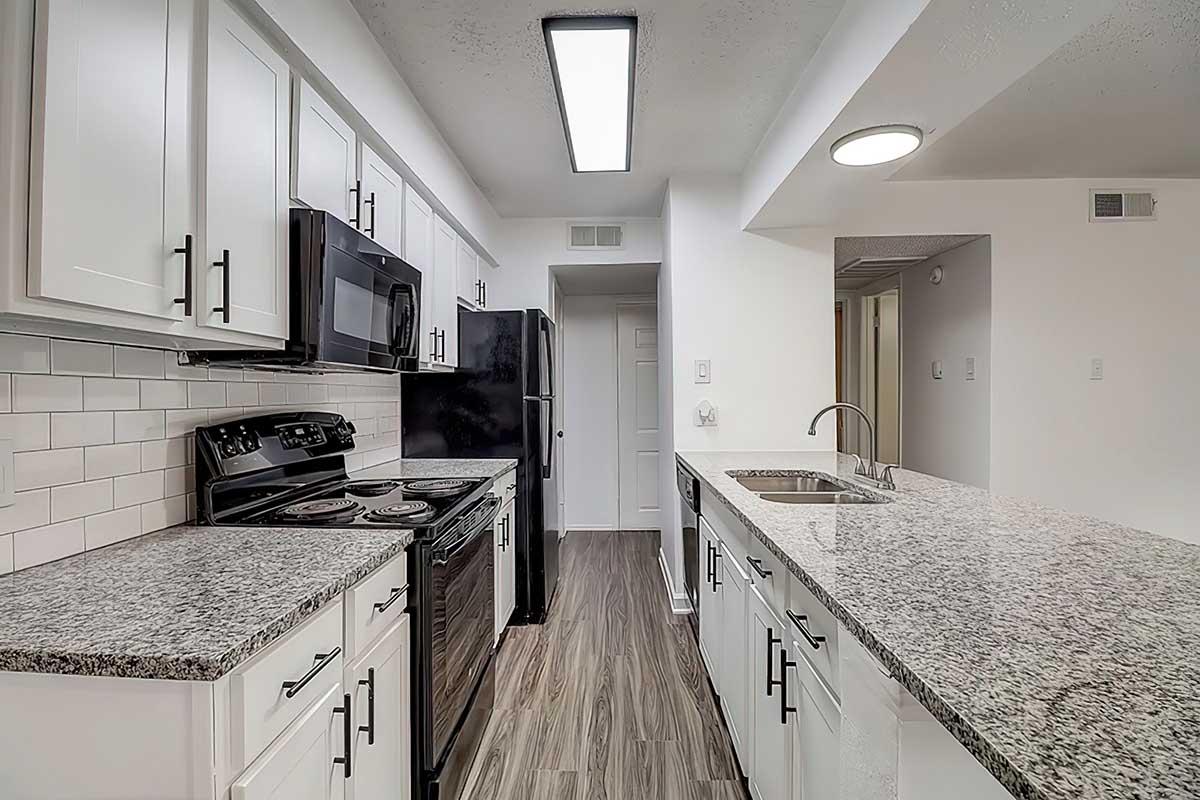 Apartment kitchen with black appliances, white cabinets, and granite counters