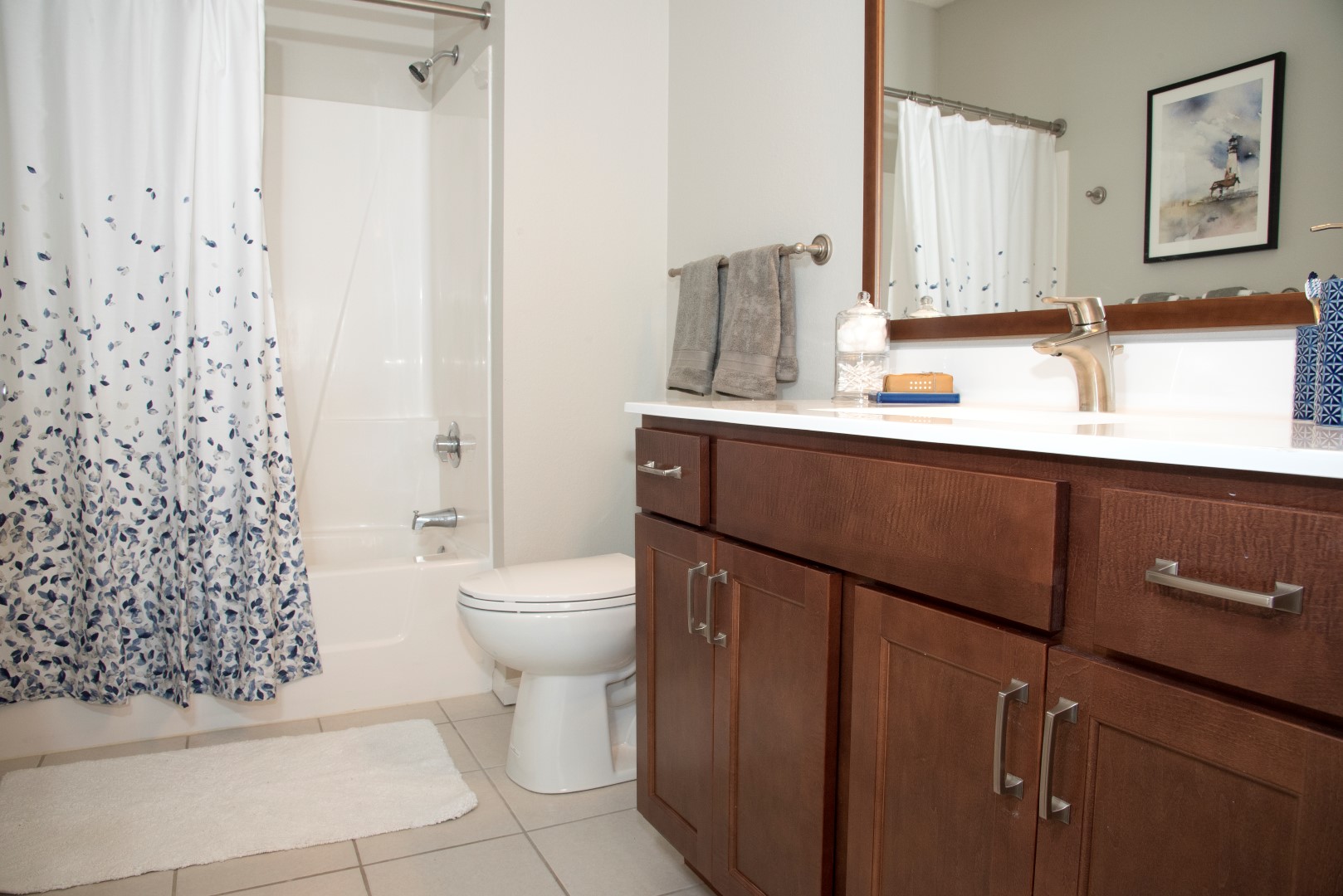 Apartment bathroom with a tub and shower, wood vanity, and framed mirror at Waterstone Place.