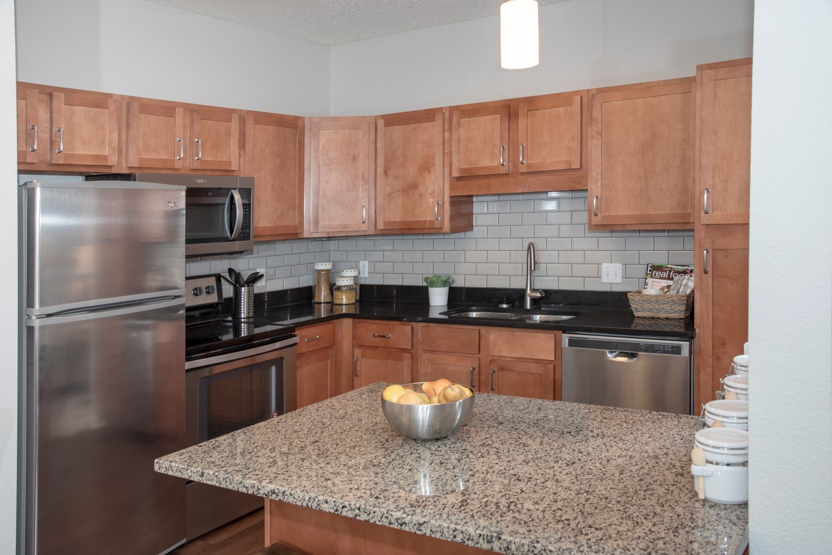 Apartment kitchen with cherrywood cabinets, granite counters, a tile backsplash, and stainless steel appliances at Waterstone Place.