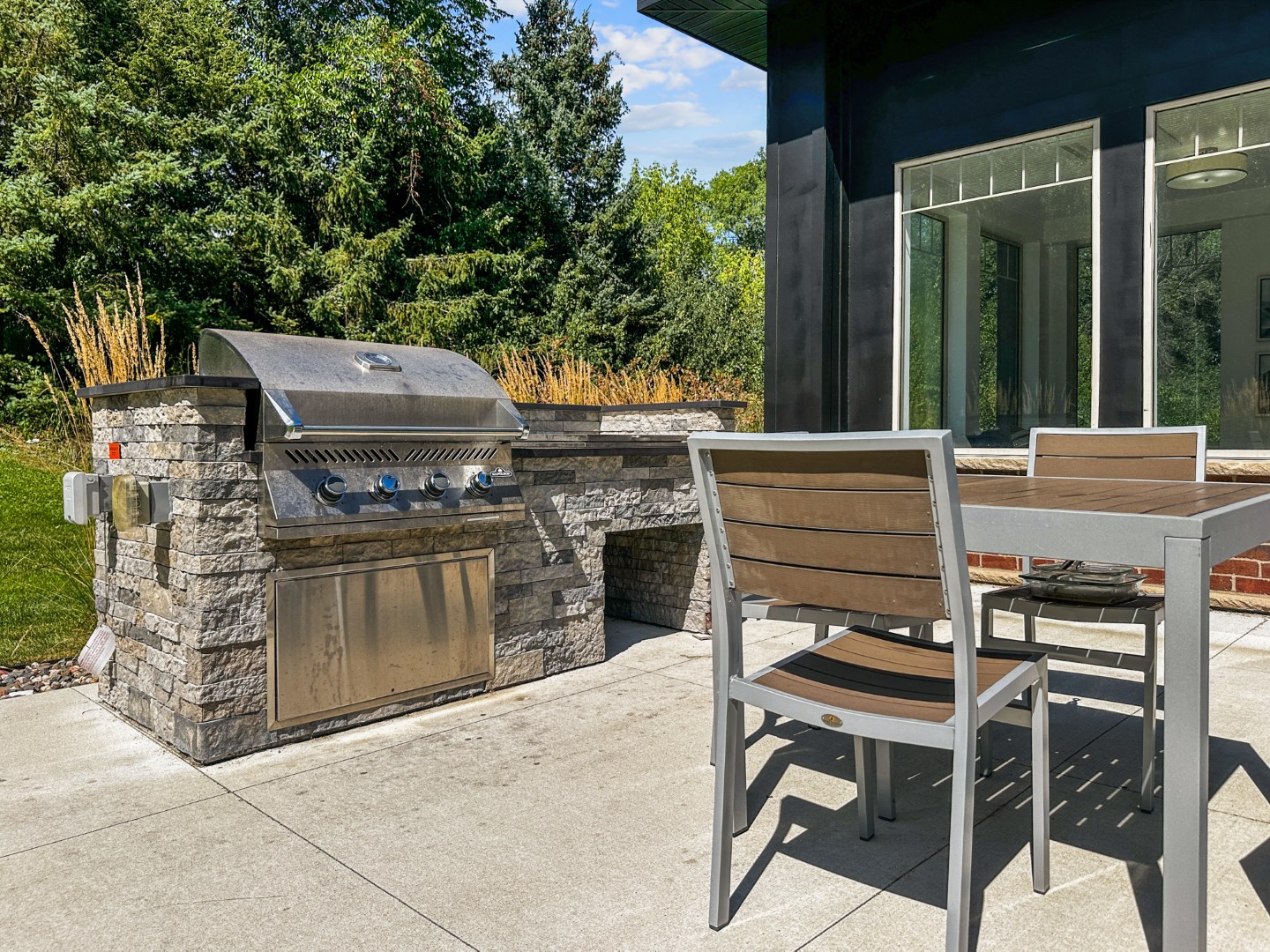Waterstone Place patio dining table beside a gas grill and surrounding landscaping.